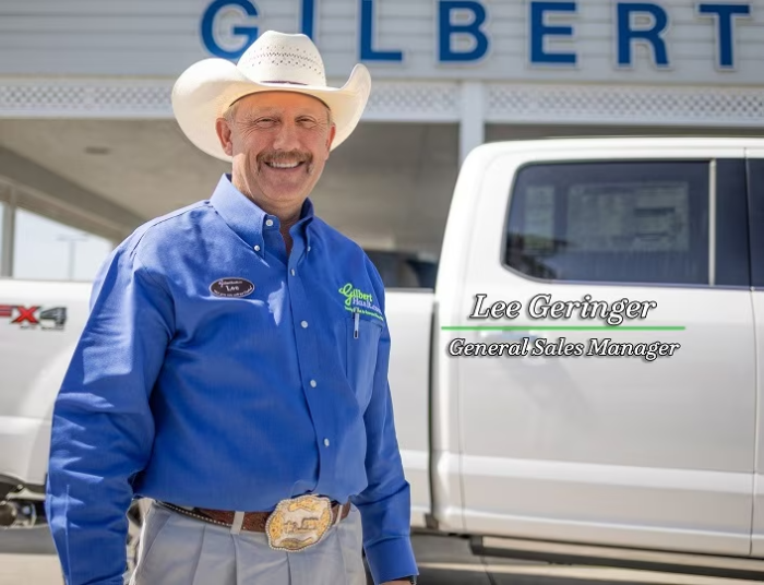 Lee Geringer, General Sales Manager, smiling in a cowboy hat and blue shirt in front of a white truck and Gilbert sign.