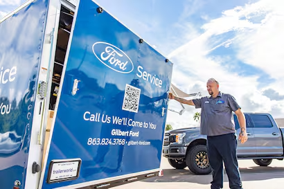 A Ford Service technician opens the back of a blue mobile service trailer with a Ford logo and contact information.